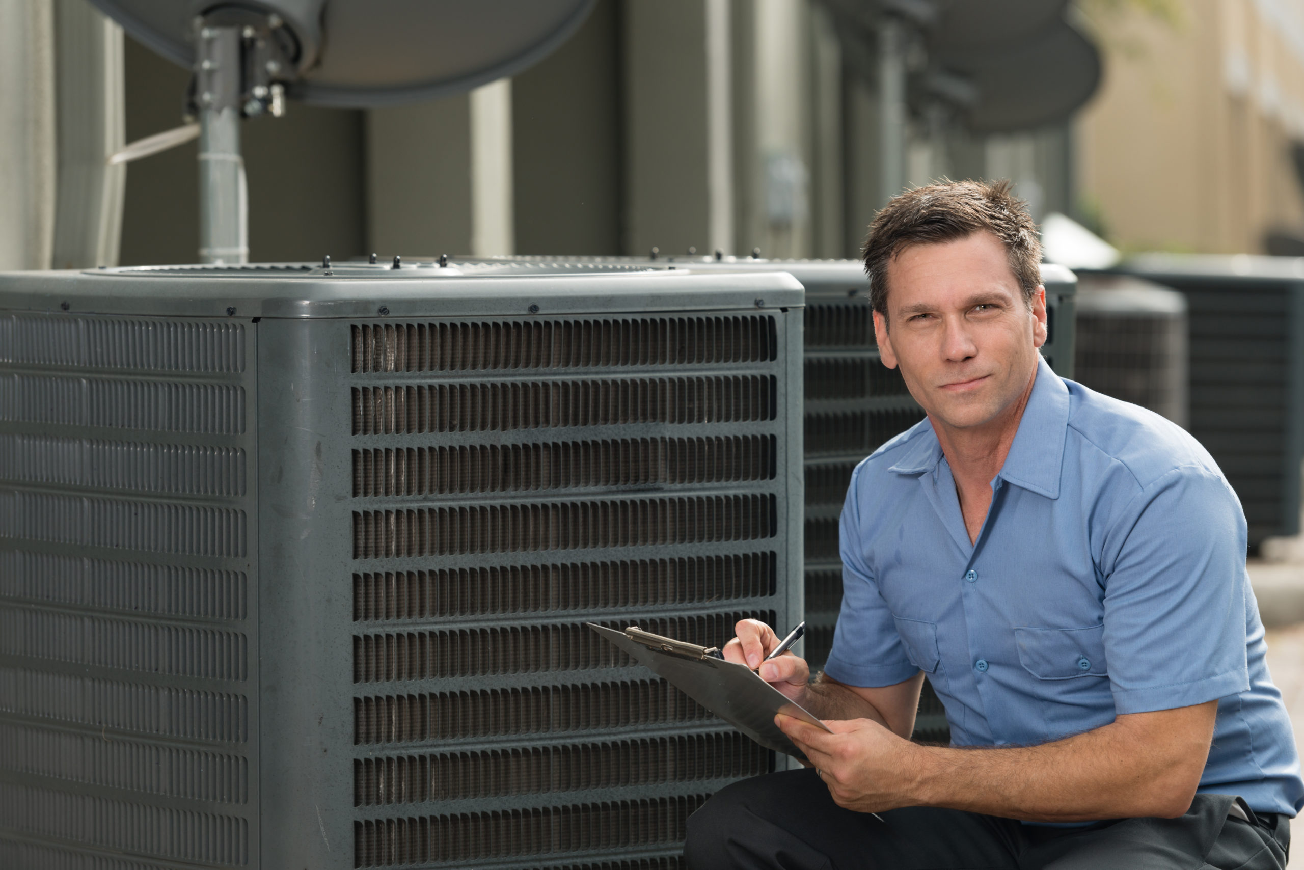 A person is inspecting HVAC unit with clipboard in hand