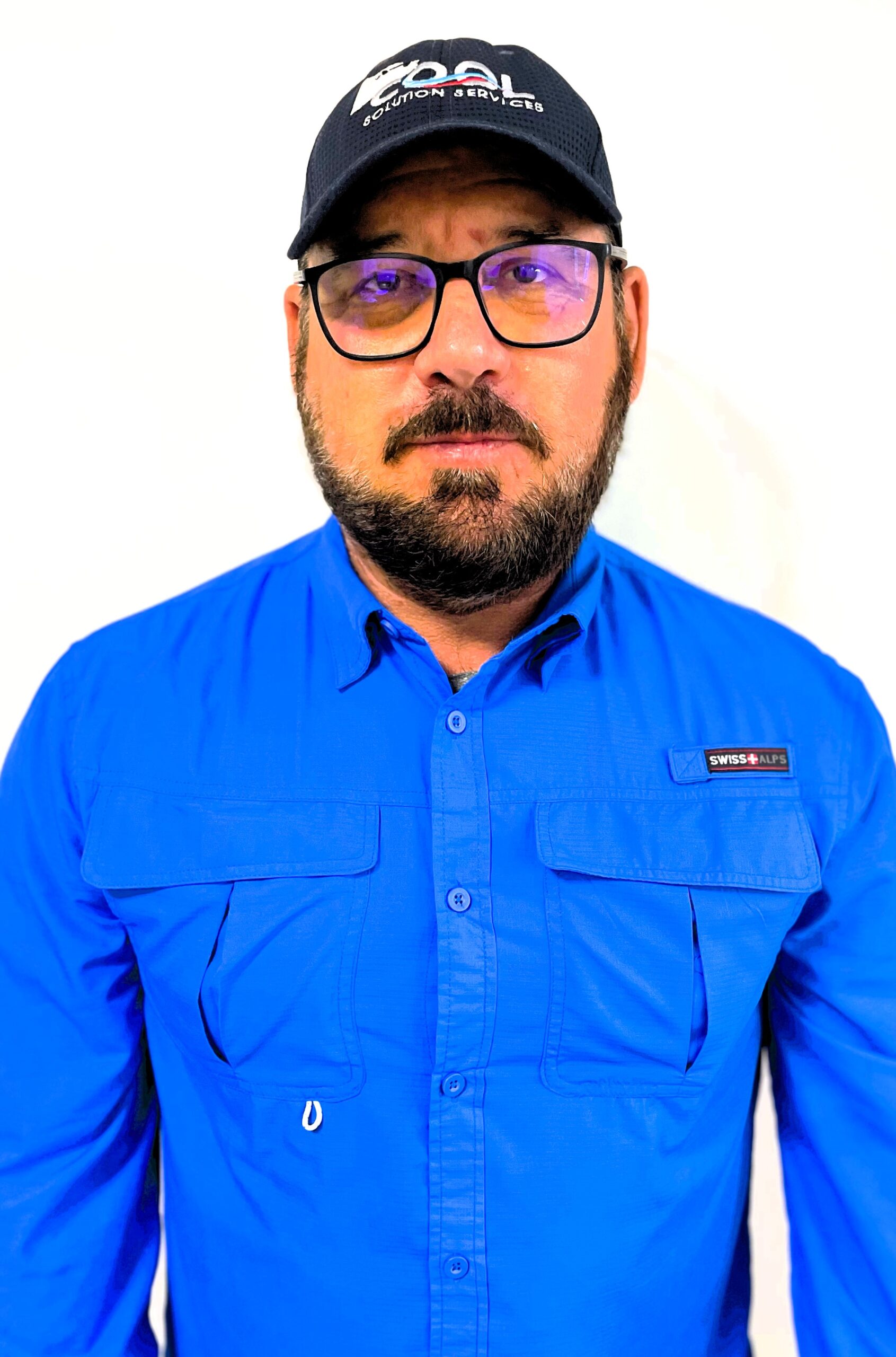 a man in blue shirt with cap and specs is smiling